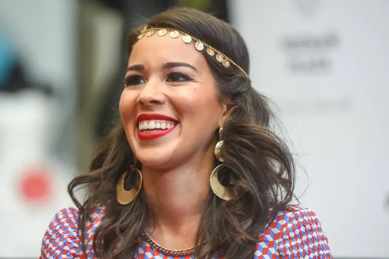 Uśmiechnięta Tamara Gonzalez Perea w złotej biżuterii i kolorowej sukience.
