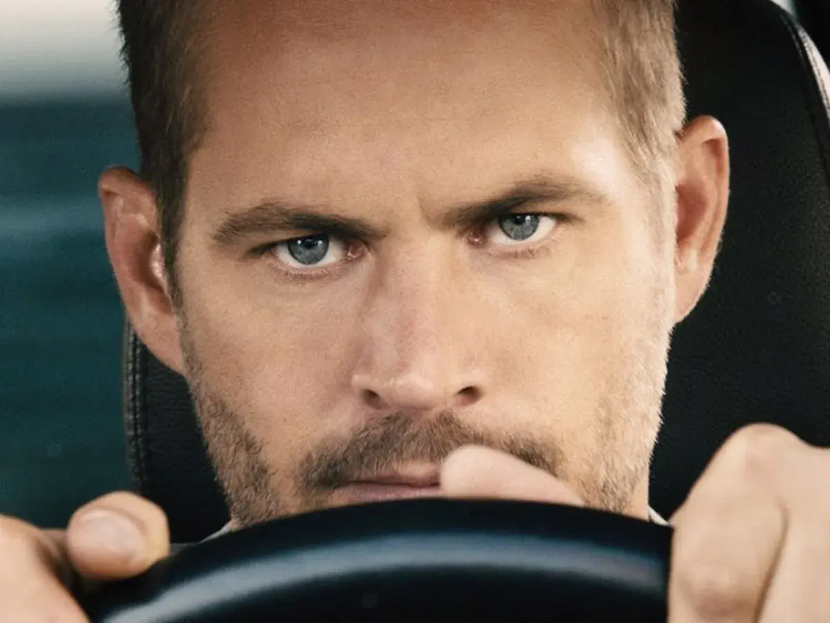 Paul Walker, gwiazda filmów o szybkich samochodach, z intensywnym spojrzeniem za kierownicą.