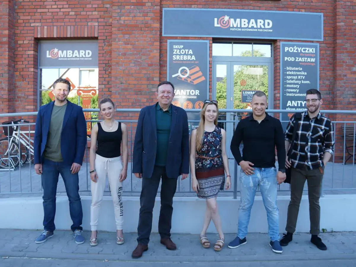Lombard życie pod zastaw obsada: uśmiechnięci pracownicy lombardu pozują przed budynkiem.