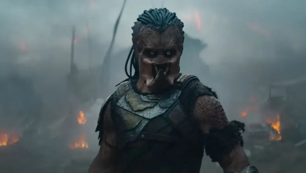 Predator w strefie zagrożenia, otoczony dymem i płomieniami. Jego groźna twarz i zbroja budzą strach.
