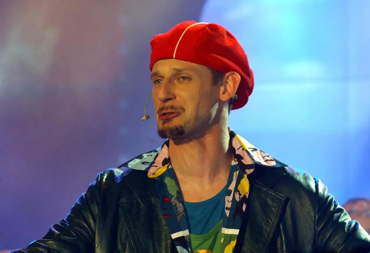 Michał Wójcik z kabaretu, w czerwonej beretce i kolorowej koszuli, na scenie.