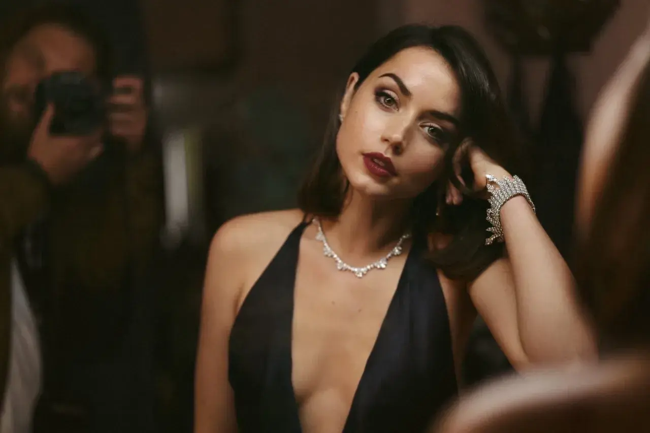 Elegancka Ana de Armas w czarnej sukni i biżuterii, jak z najlepszych filmów. W tle widać fotografa.