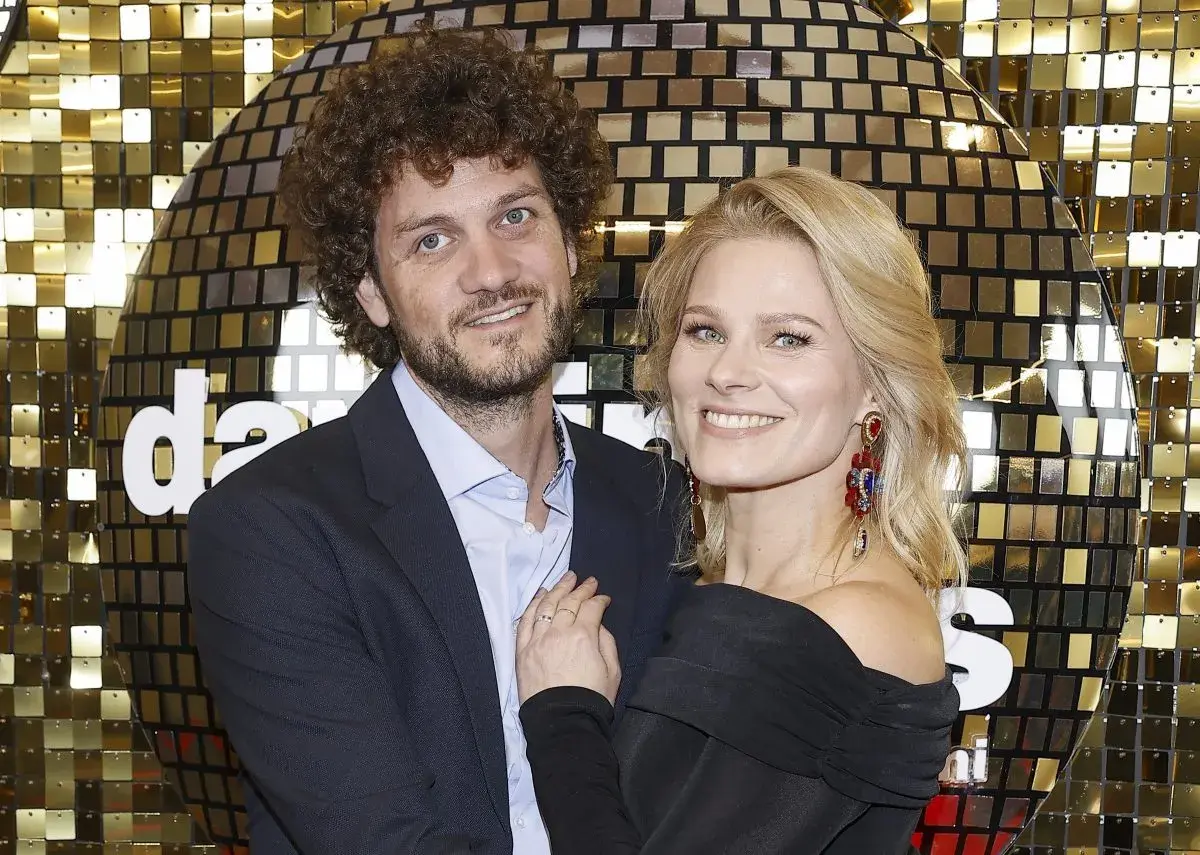 Anna Głogowska z partnerem pozują na tle błyszczącej, złotej ściany.