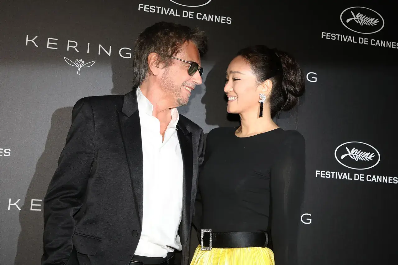 Jean-Michel Jarre i jego żona, Gong Li, uśmiechają się do siebie na tle napisu "Festival de Cannes".