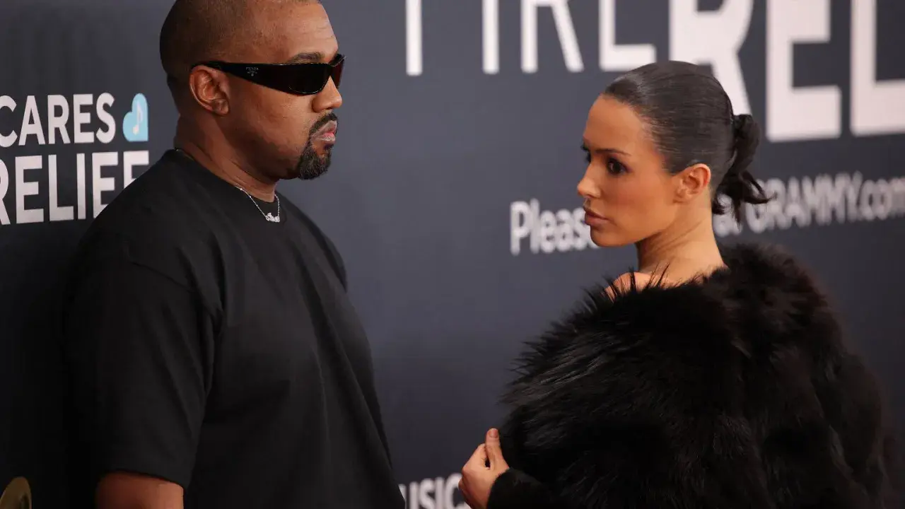 Kanye West i Bianca na ściance. Kanye w czarnym t-shircie i okularach, Bianca w futrzanym płaszczu.