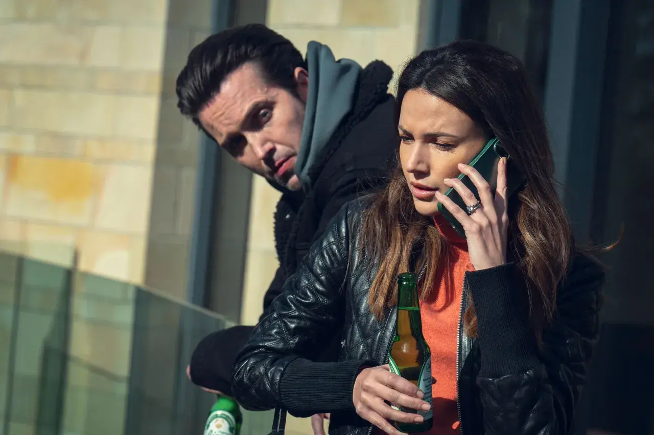 Kobieta rozmawia przez telefon, trzymając piwo. Mężczyzna za nią patrzy z podejrzliwością. Już mnie nie oszukasz.