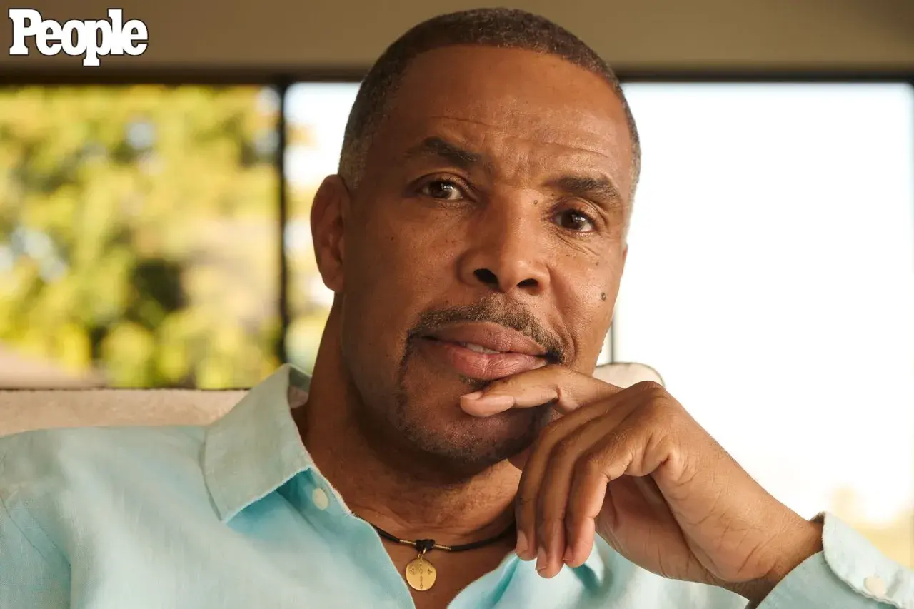 Eriq La Salle, zamyślony, opiera podbródek na dłoni. Ma na sobie błękitną koszulę i naszyjnik.