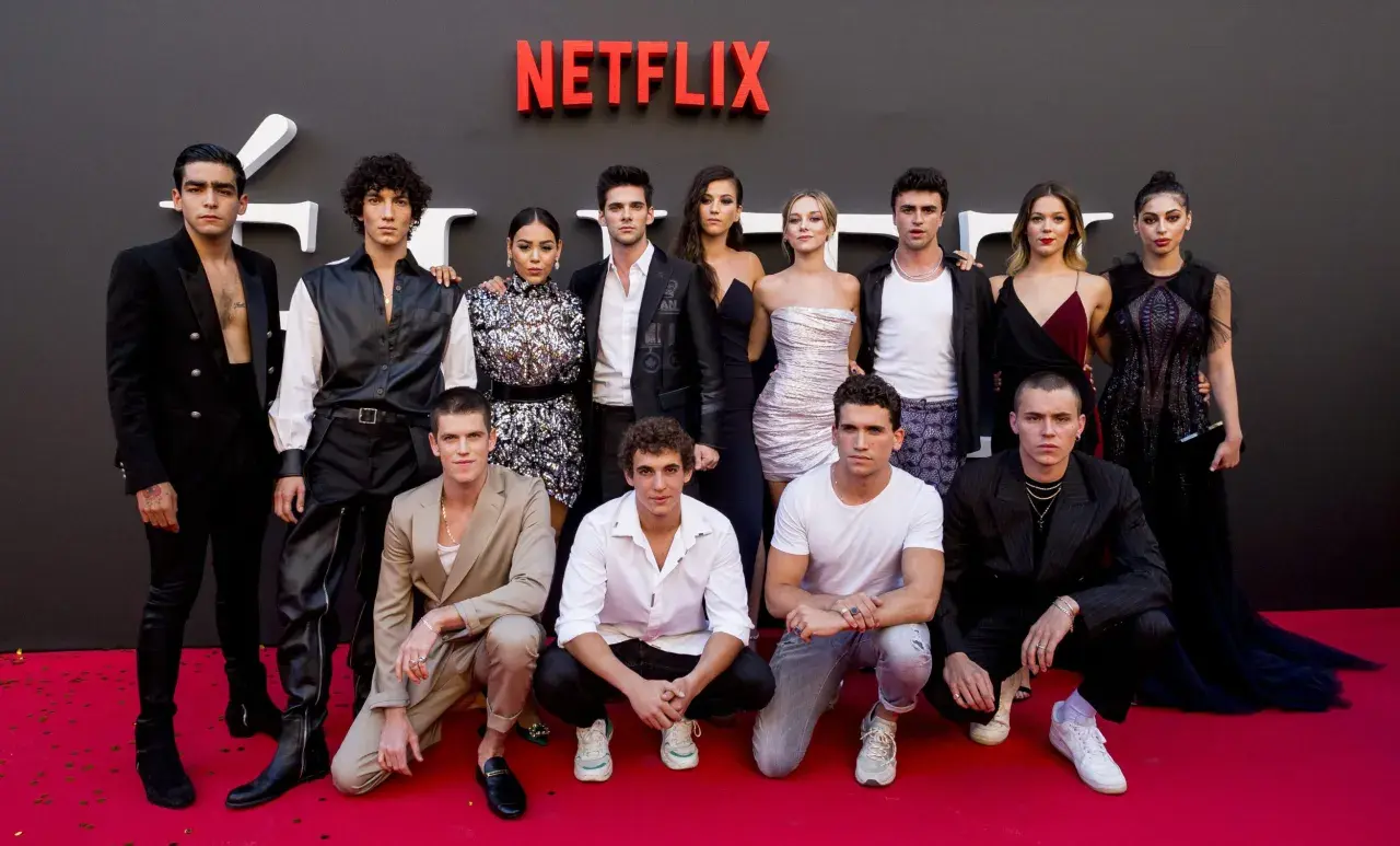 Cała obsada serialu "Szkoła dla elity" pozuje na czerwonym dywanie przed logo Netflix.