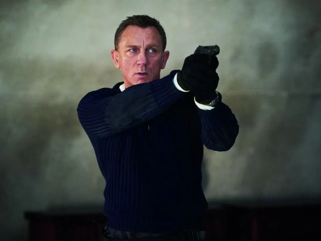 Daniel Craig w roli Jamesa Bonda, gotów do akcji z pistoletem w dłoni. Scena jak z najlepszych filmów o Jamesie Bondzie.