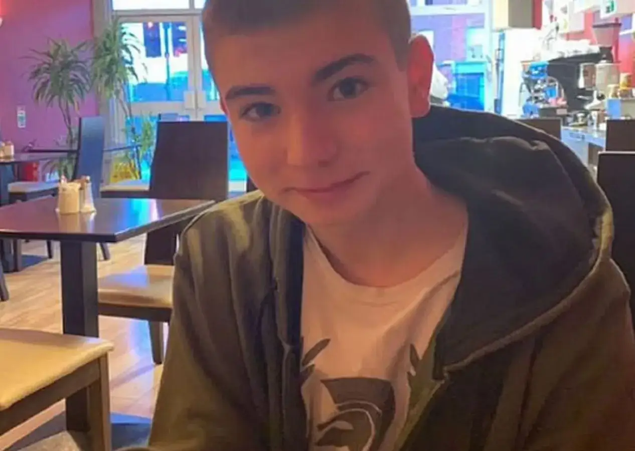 Młody mężczyzna, syn Sinead O'Connor, siedzi w kawiarni, ubrany w zieloną bluzę z kapturem i białą koszulkę.