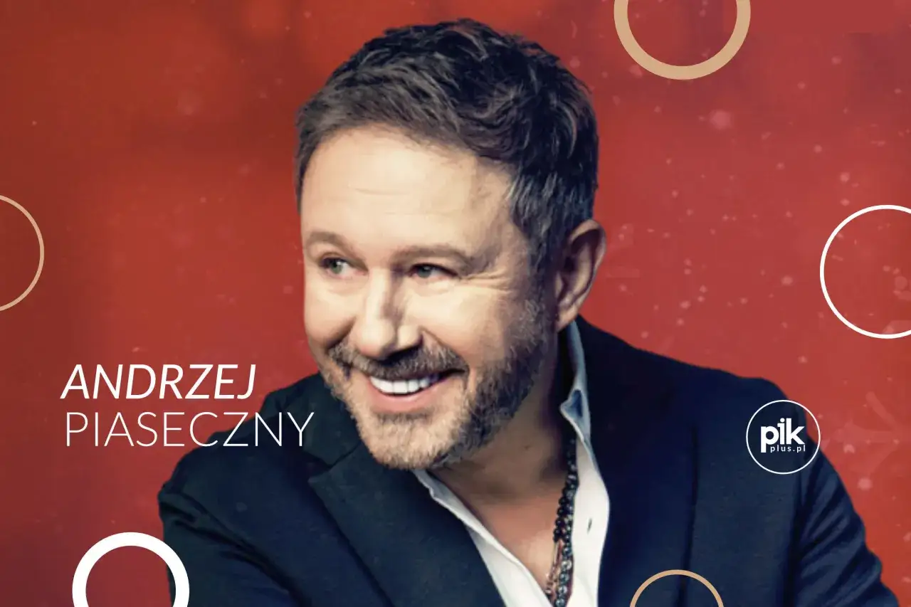 Uśmiechnięty Andrzej Piaseczny na czerwonym tle. Choć nie widać jego żony, jego spojrzenie sugeruje szczęście.
