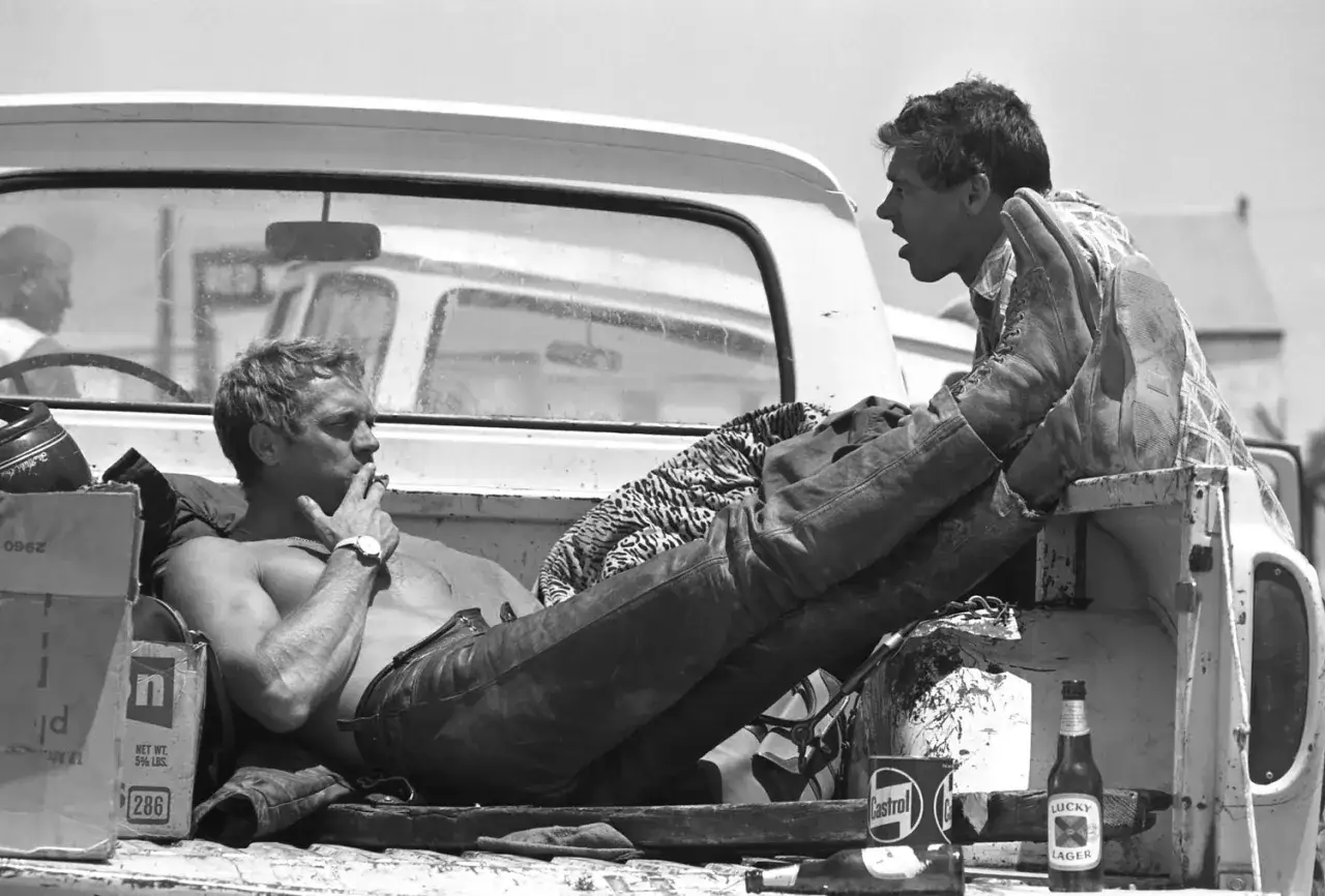 Steve McQueen, gwiazda swoich filmów, odpoczywa w pace pickupa, paląc papierosa. Obok butelka piwa Lucky Lager.