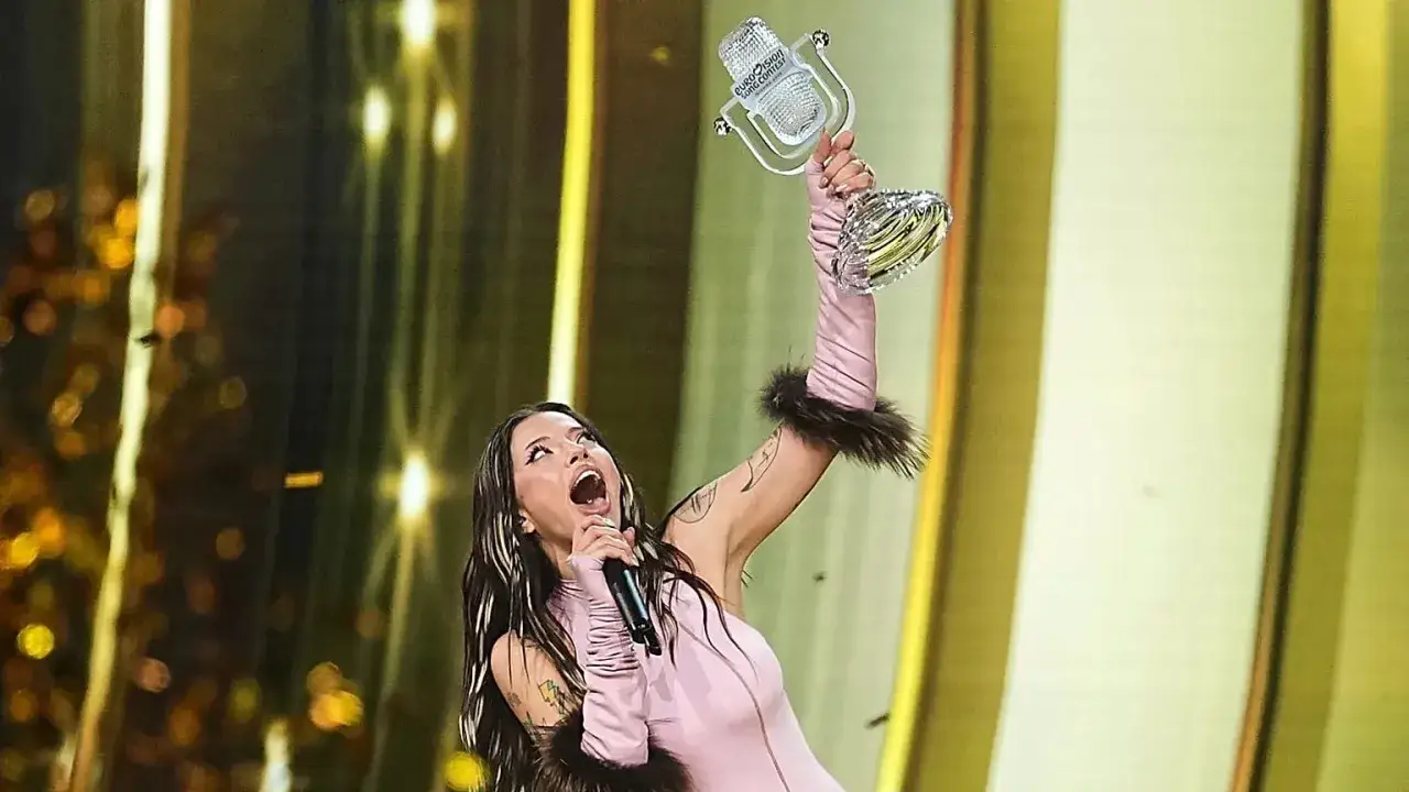 Zwyciężczyni Eurowizji z pucharem w dłoni, w r&oacute;żowej kreacji z futrzanymi rękawami, świętuje triumf.