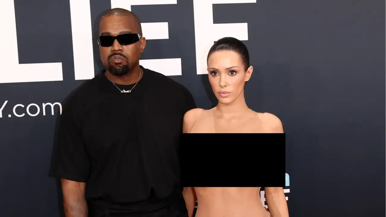 Kanye West i Bianca na ściance. Kanye w czarnym t-shircie i okularach, Bianca w cielistej kreacji.